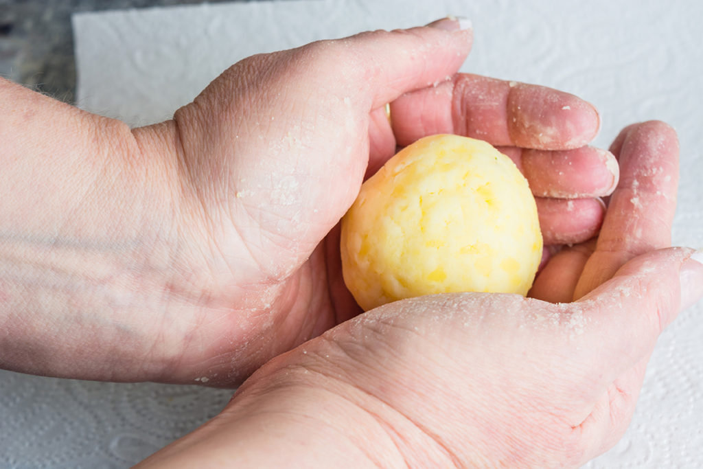 Fertigen eines Kartoffelkloßes, zwischen den Handflächen gerollt.