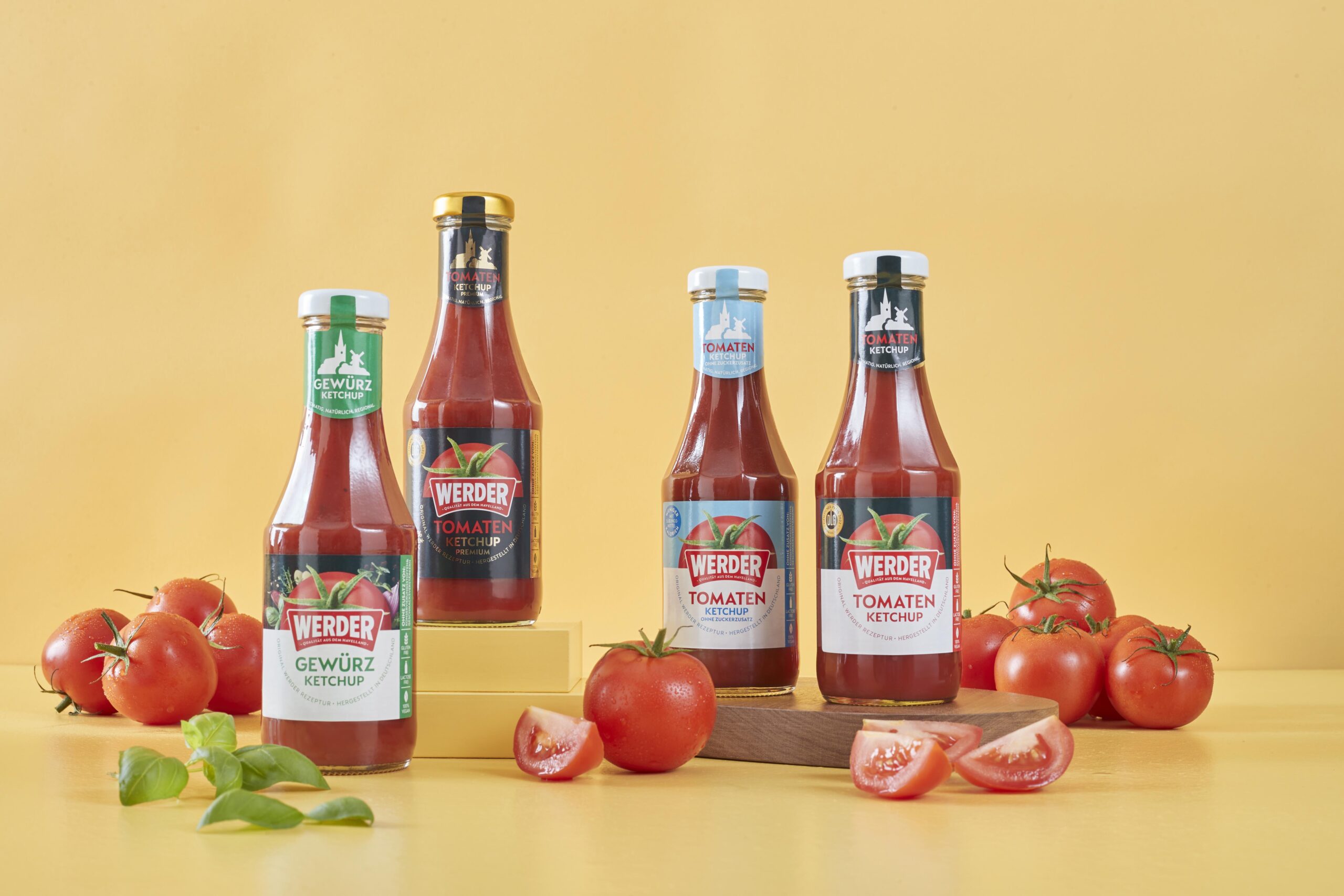 Vier verschiedene Sorten Werder Ketchup in Flaschen vor einem gelben Hintergrund.