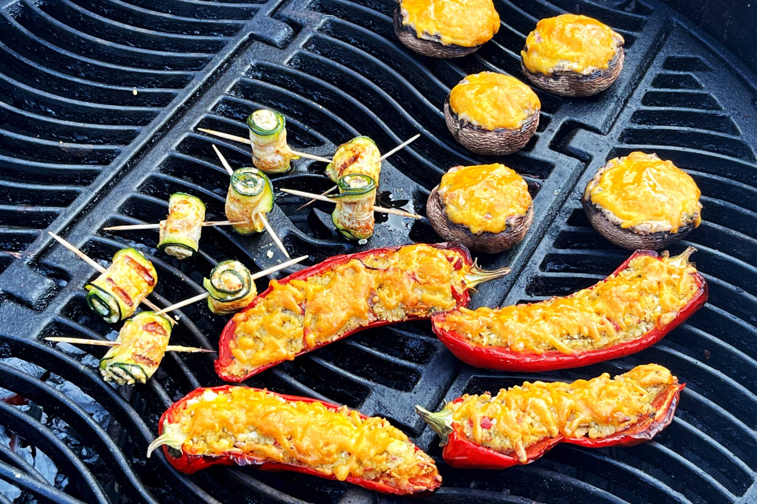 Champignons (gefüllt mit einer Frischkäse-Creme und überbacken mit Cheddar), Zucchini-Röllchen mit Feta-Füllung und Spitzpaprika mit Couscous-Füllung (und mit Cheddar überbacken) auf dem Grill.