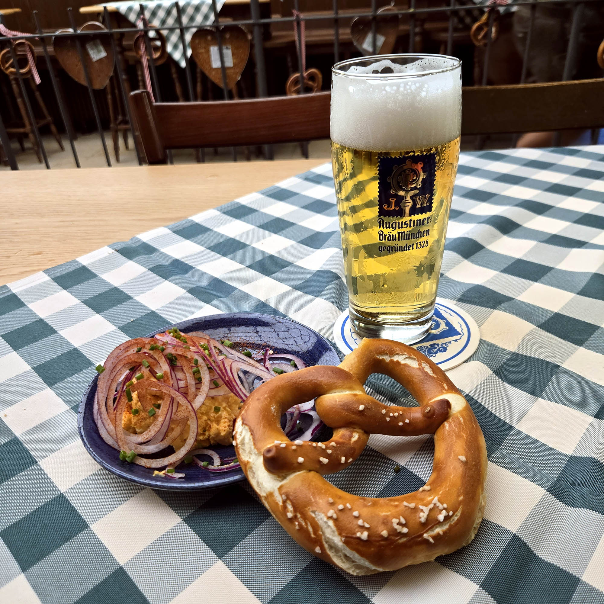Bild mit Obazda, Augustiner Bräu Bier und einer Brezel auf einer karierten Tischdecke in einem Brauhaus